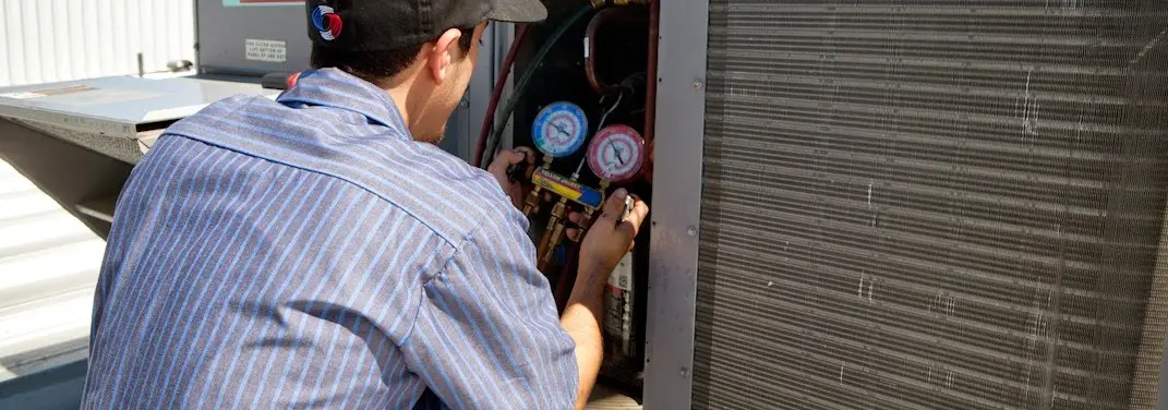 HVAC technician servicing a condenser unit in North Versailles